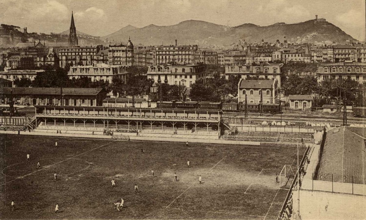 Postal antigua de Atocha con un partido en juego, una tribuna de madera y San Sebastián detrás