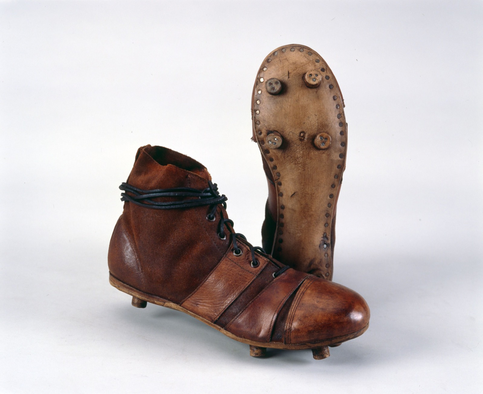Botas de cuero marrón de caña alta, una de perfil y otra de pie con los tacos de la suela a la vista