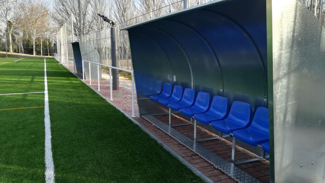 Banquillo azul junto a la banda de un campo municipal de césped artificial recién instalado