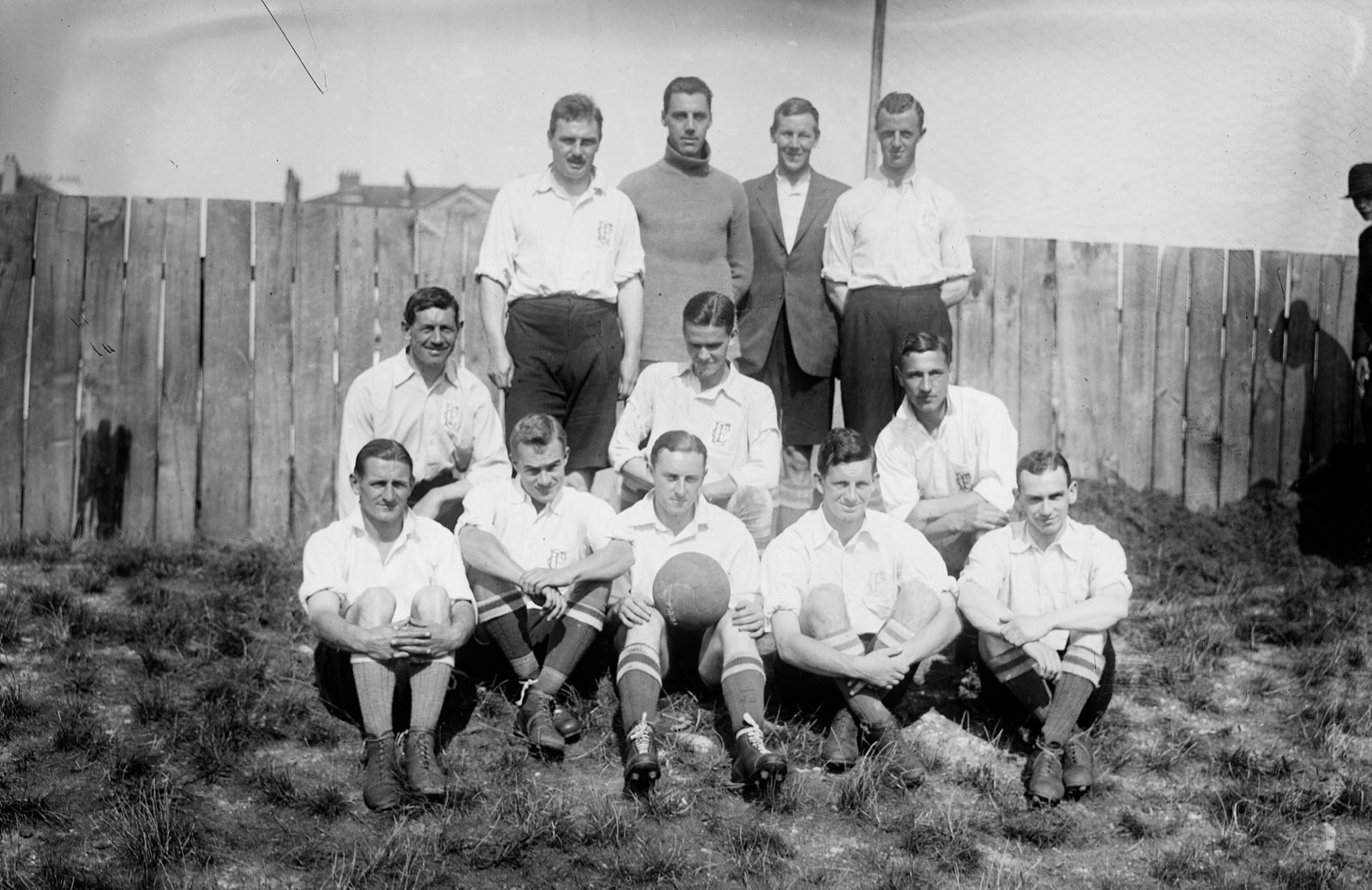Jugadores del Corinthian en 1921 con camisa blanca de cuello abierto, junto a una valla de madera